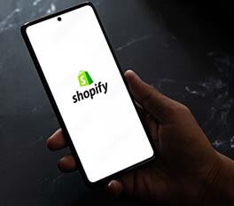 image of someone holding a mobile phone with Shopify on the display